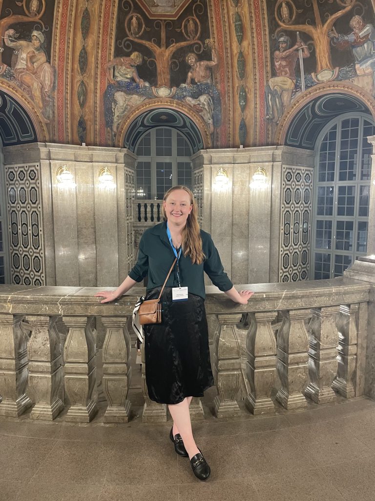 Emily stands in the stairwell of the Dresden Town Hall with a decorative domed ceiling behind her.