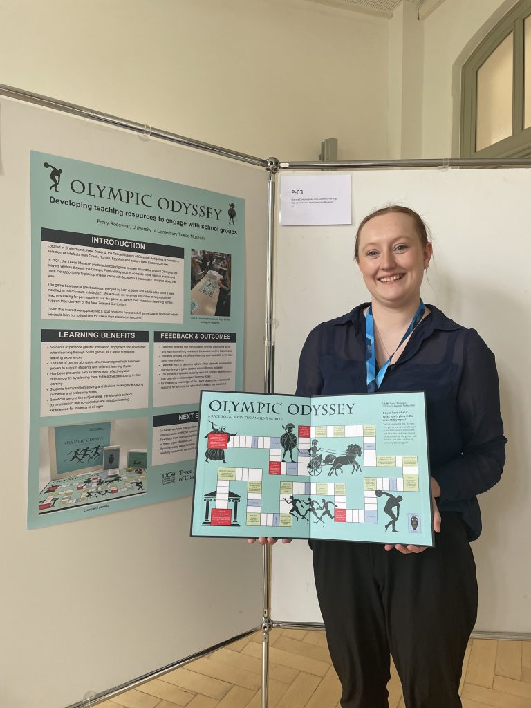 Emily holds a copy of the Olympic Odyssey game in front of her conference poster.