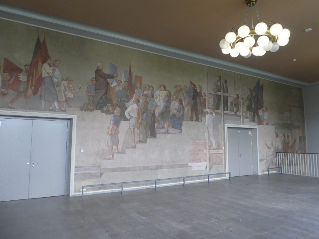 Foyer of lecture hall with mural on the wall of citizens during the german Democratic Republic.